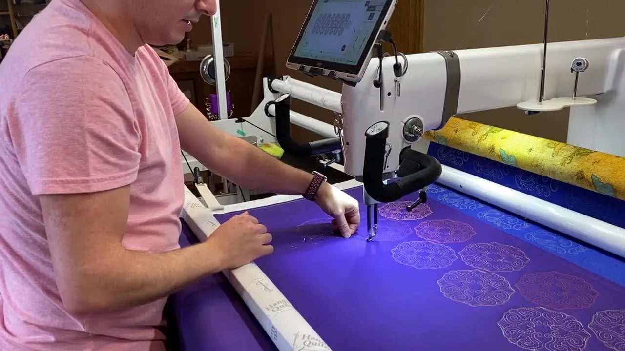 A close-up of the machine stitching a glitter thread design on dark blue fabric, showing the high-sheen effect in motion.