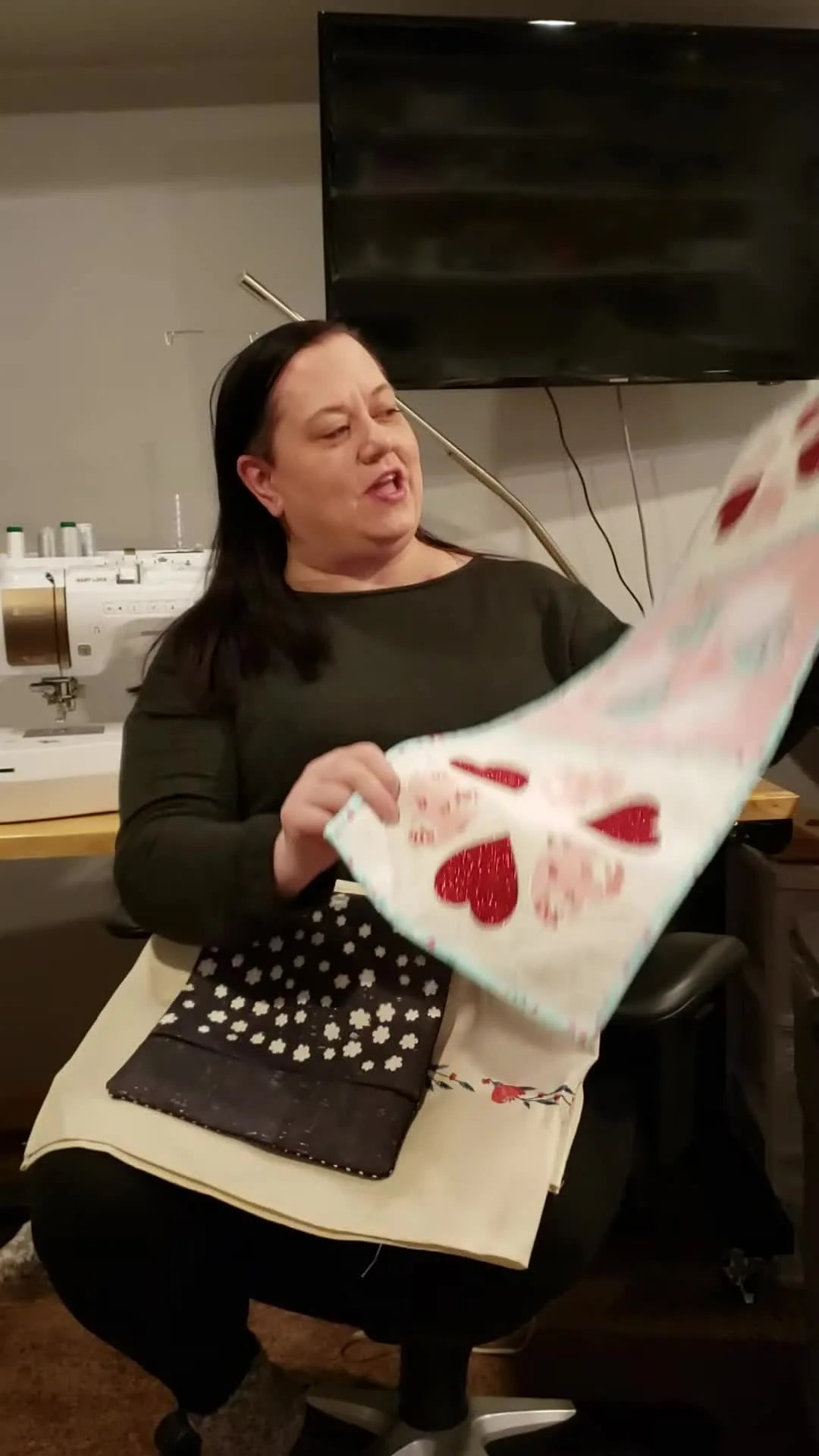 Kimberly holds up a heart-themed table runner featuring glitter heat transfer vinyl integrated with embroidery stitching.