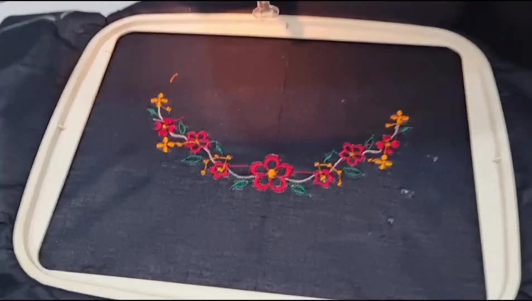 A finished curved floral neckline embroidery stitched on dark fabric, trimmed clean with no visible jump stitches.