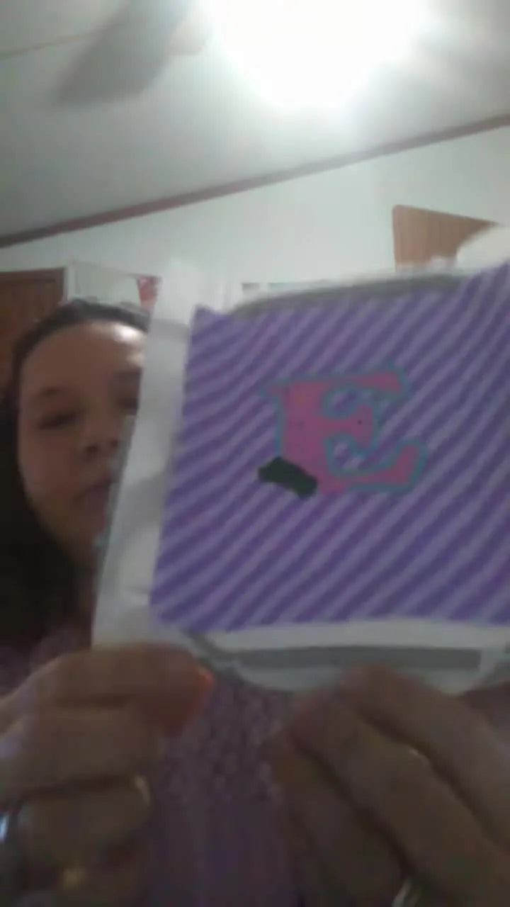 A close-up of a hooped appliqué letter E with a finished green leaf on purple striped fabric, ready for the next leaf and carrot steps.