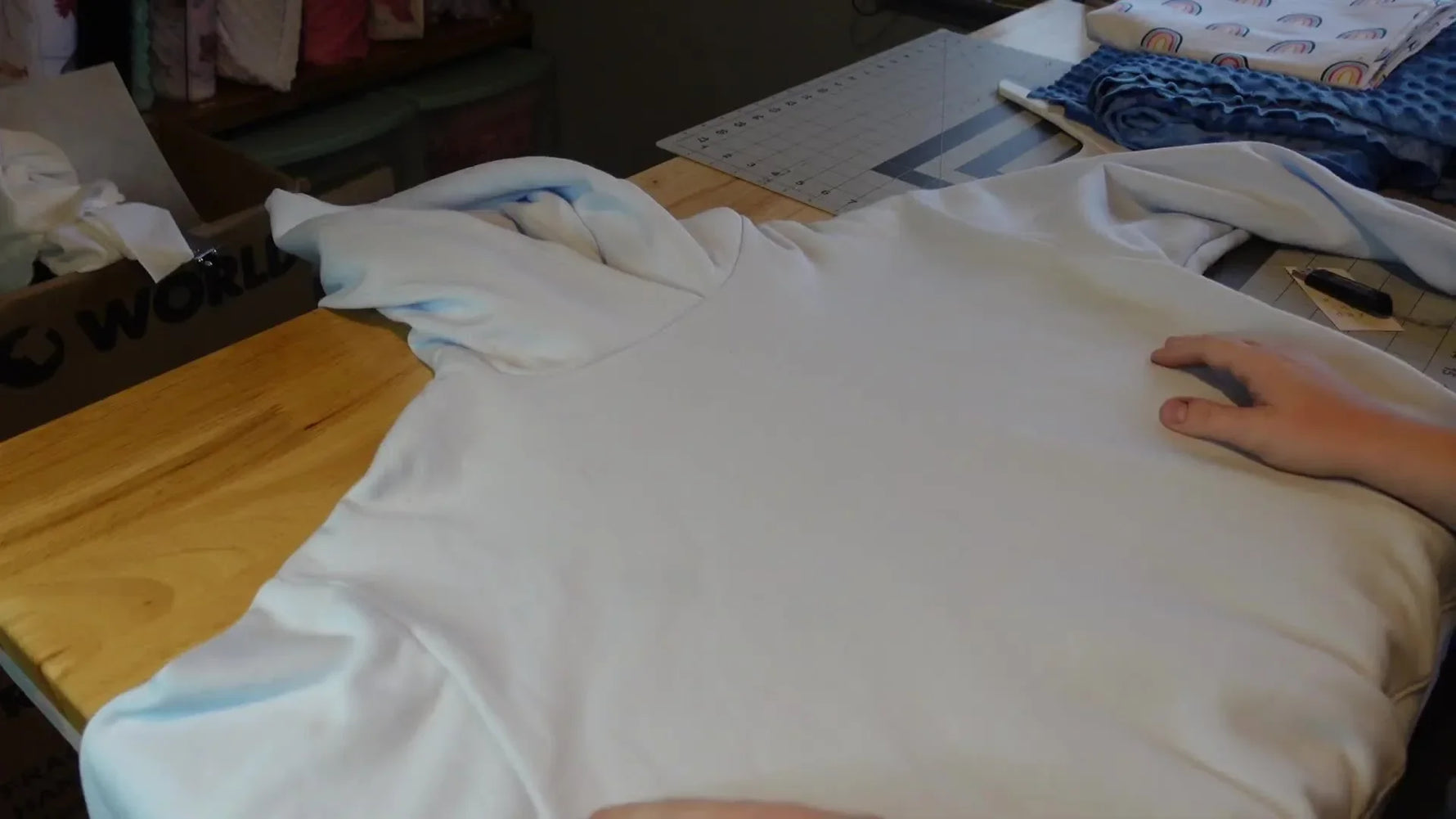 Woman preparing a light blue sweatshirt for embroidery on a wooden table.