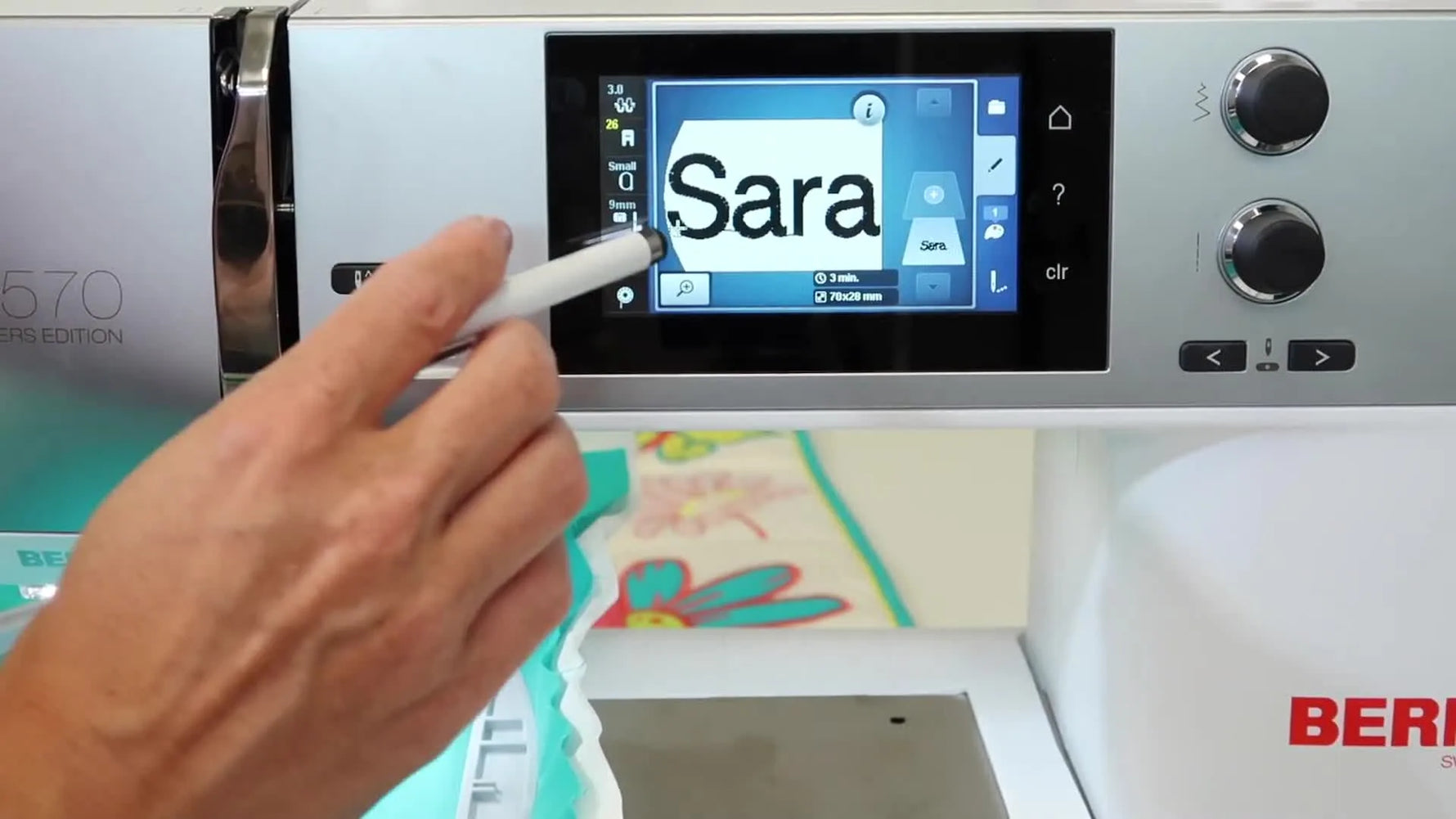 The BERNINA 570 QE screen shows the name “Sara” positioned inside the hoop boundary after confirming the text entry.
