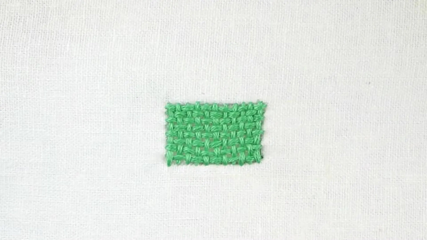 A small square shape on white fabric fully embroidered with a green basketweave stitch, showing a distinct woven texture.