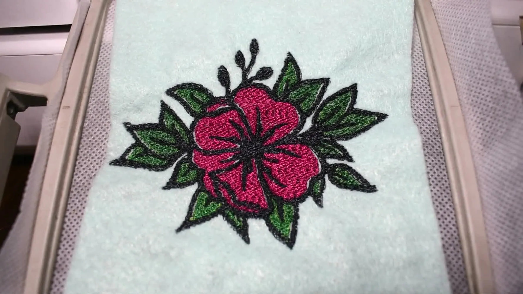 Top-down view of the finished floral embroidery still in the hoop on light blue felt, ready for quality inspection.