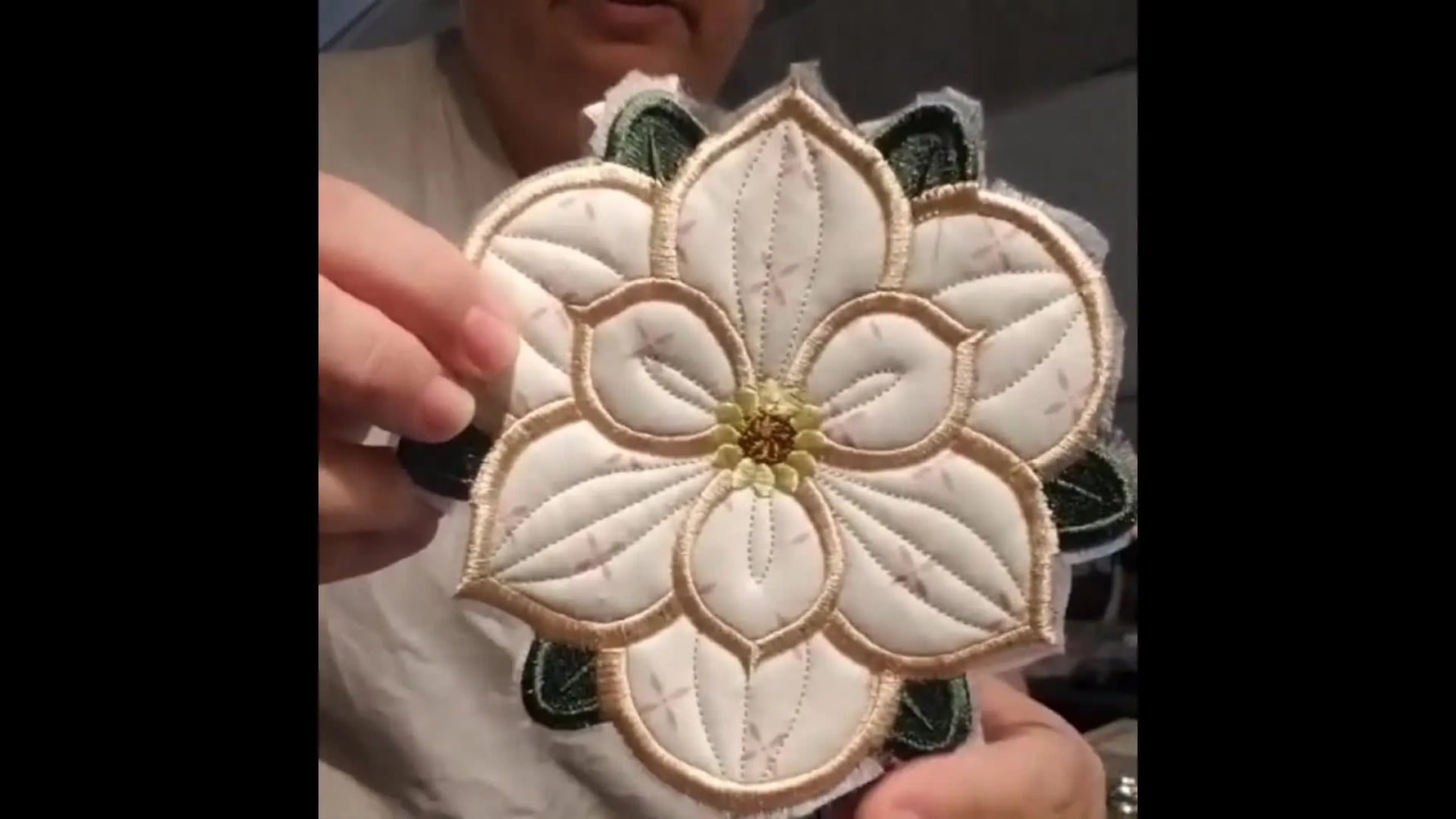 A finished reversible Magnolia trivet is held up to show the clean satin border and crisp petal details.
