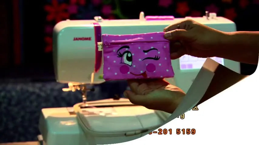 A finished pink in-the-hoop zipper pouch with a winking face design held close to the camera.