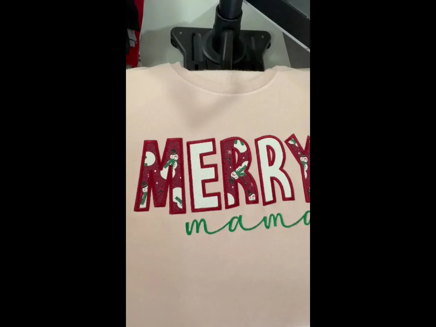 A close-up reveal of the finished “MERRY mama” appliqué sweatshirt showing clean satin edges and textured fabric fill.