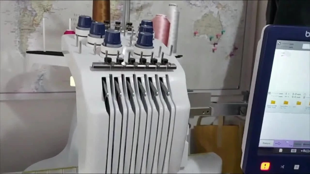 A Brother PR670E stitches white running-stitch lettering onto a folded pink triangle label held with a floating stabilizer setup.