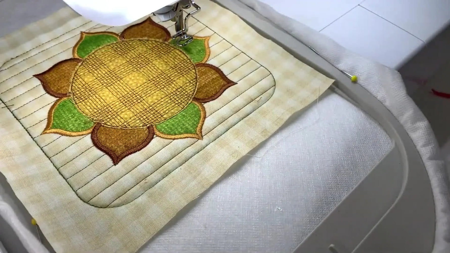A close-up of the embroidery machine satin-stitching the sunflower center with a plaid detail, showing clean coverage and stable fabric control.