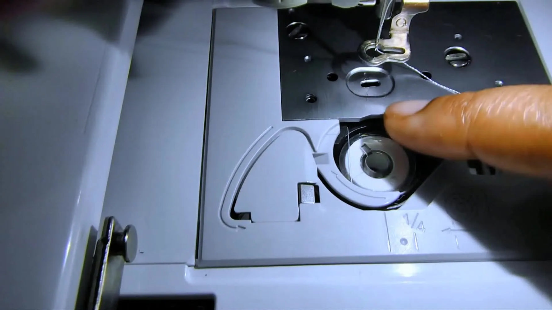A close-up shows a finger holding the drop-in bobbin firmly in place while the thread tail is pulled into the guide—an easy-to-miss move that prevents instant nesting.