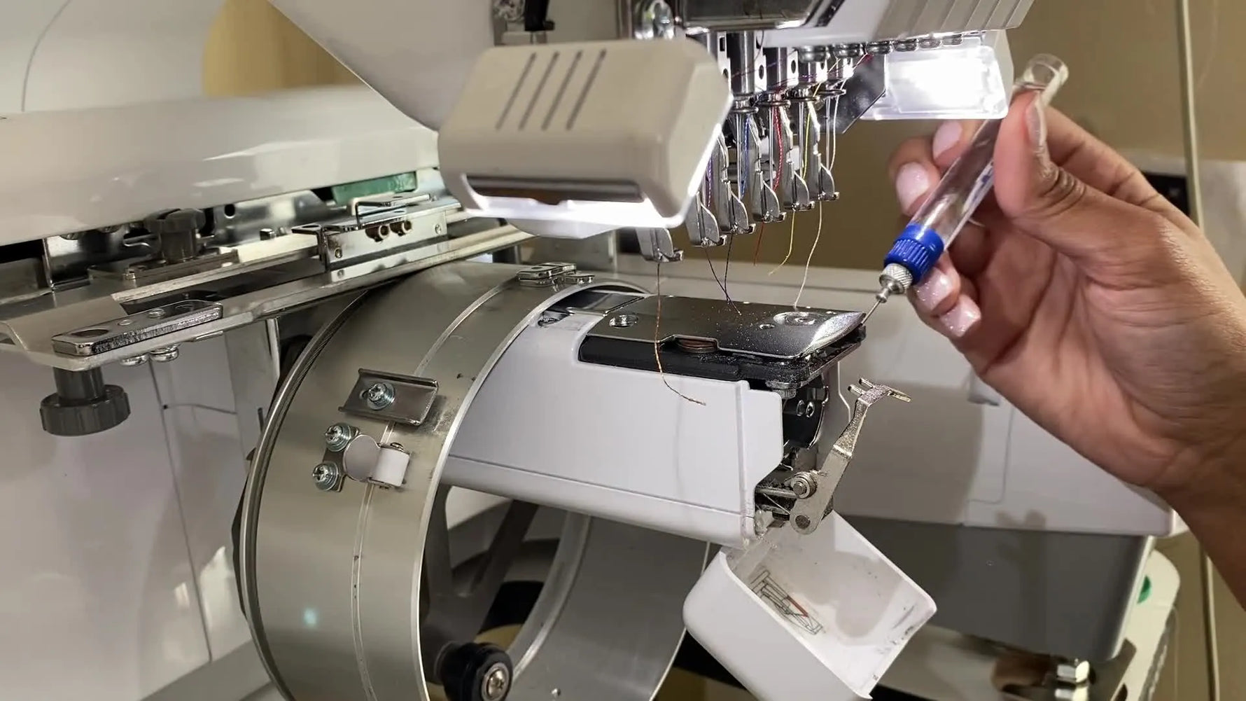 An extreme close-up shows a precision oil pen placing a single drop of oil onto the rotary hook race on a Brother PR-series machine.