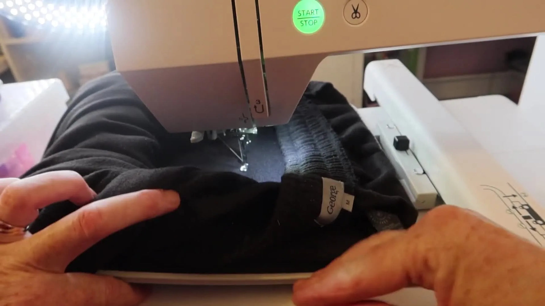 A close-up of the Janome Memory Craft 400E stitching white text onto black sweatpants during the main stitch-out.