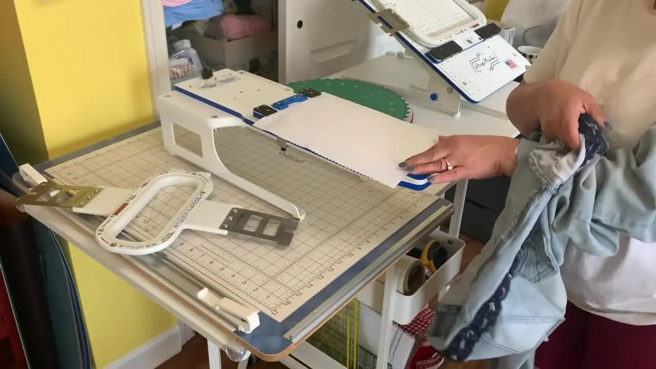 A hand reaches inside a denim pant leg to hold cutaway stabilizer steady while the jeans are positioned on a magnetic hoop station for clean, centered embroidery.