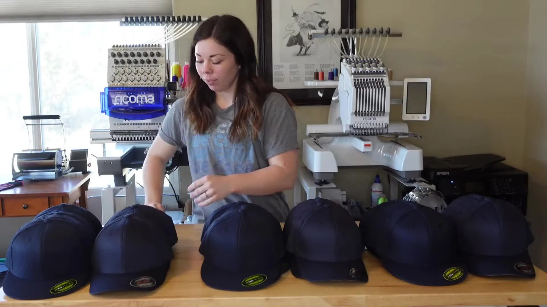 Woman holding a white card with 'The Carriage House' logo above a row of navy blue hats.