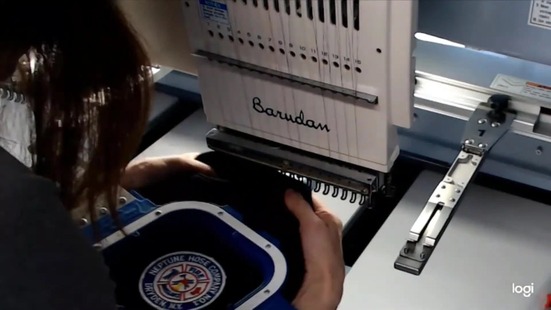 A Barudan multi-needle embroidery machine stitches a white tack-down run around a patch edge held securely in a magnetic hoop.