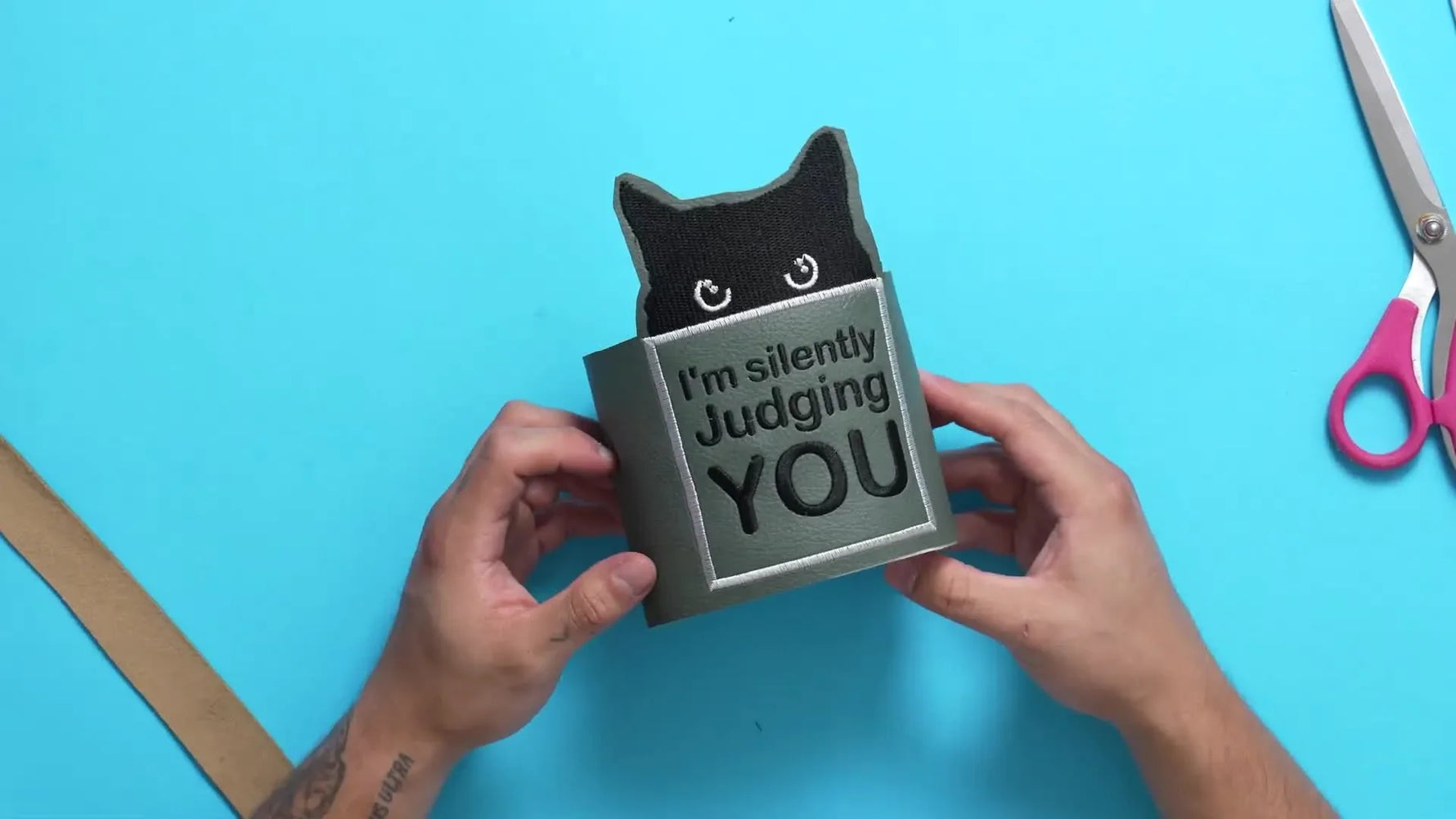 A close-up of the finished faux leather “Judging Cat” wrap fastened around a toilet paper roll with the text visible.
