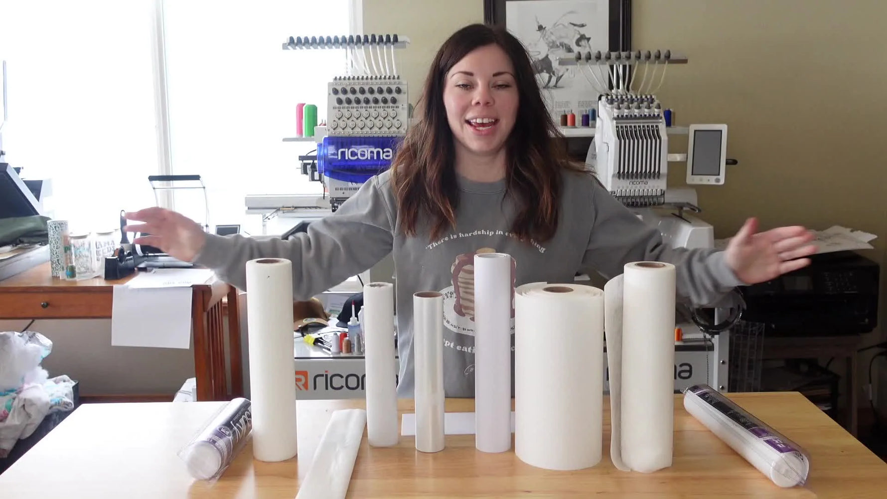 Presenter standing behind a table with various rolls of embroidery stabilizers, arms spread.