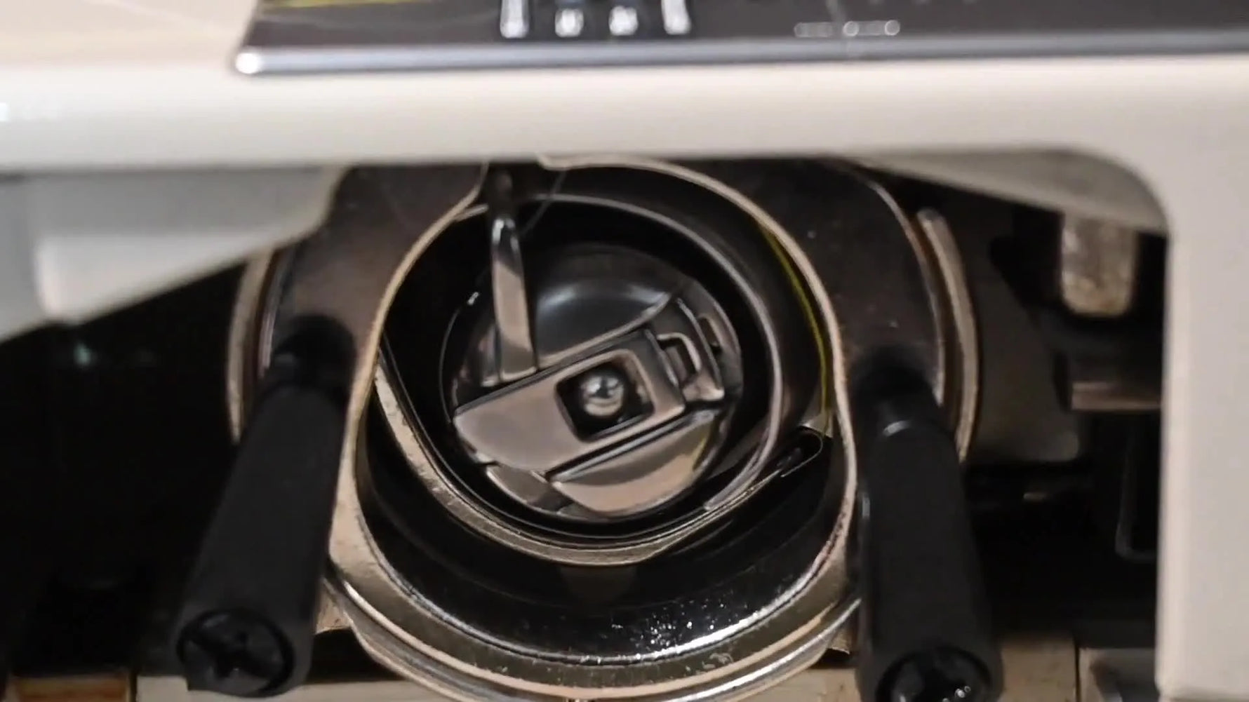 An extreme close-up of the yellow top thread looping around the bobbin case inside the sewing machine.