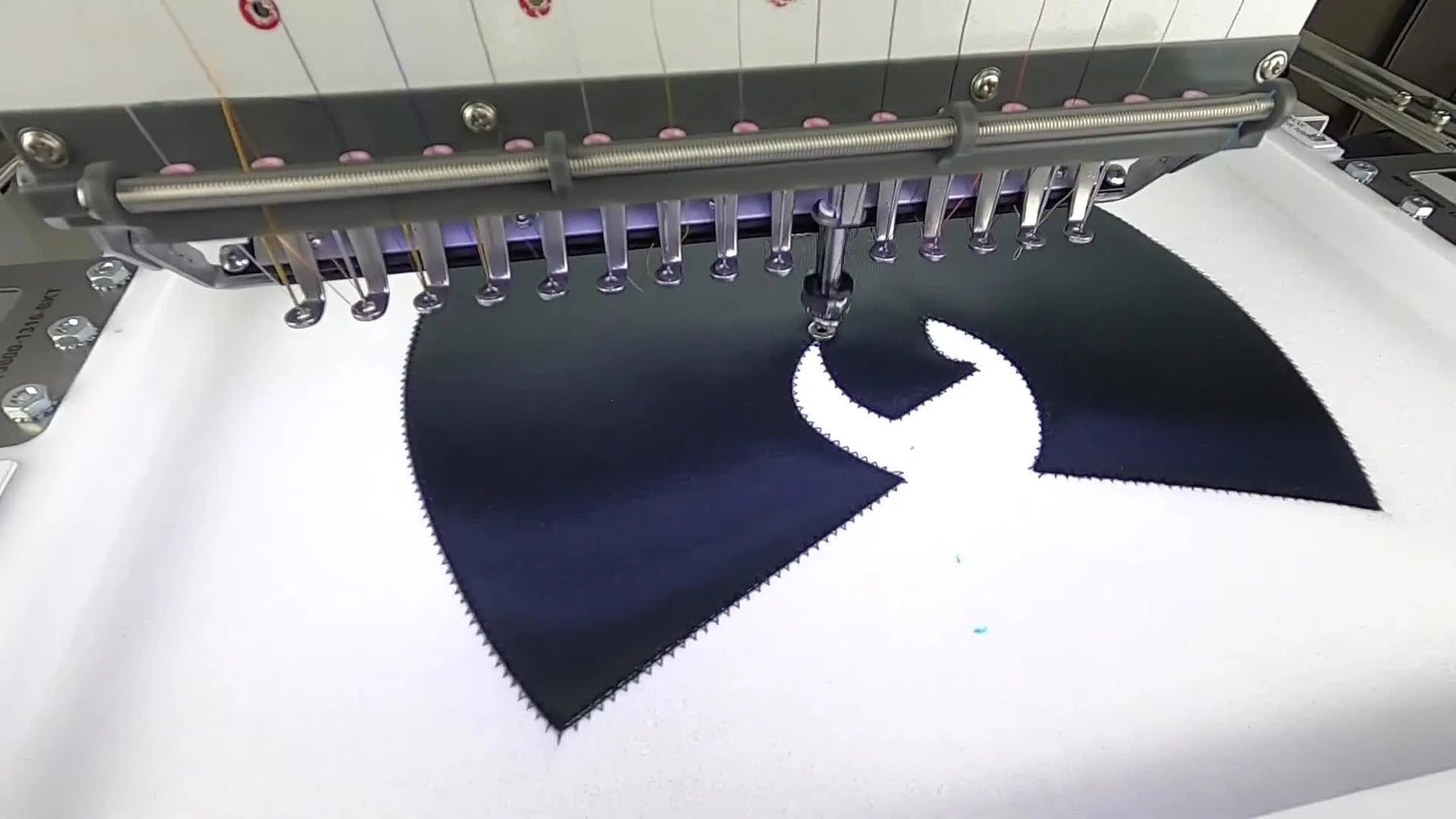 A close-up of the embroidery machine forming the zigzag tackdown stitch that locks the appliqué in place before the satin border.