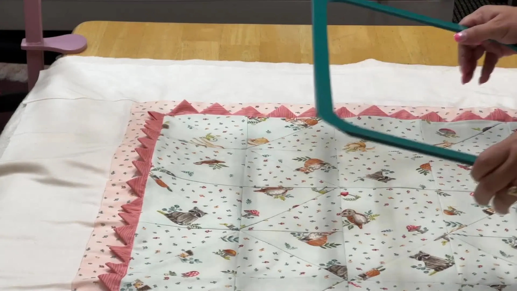 Hands align a green magnetic hoop top frame over a quilt sandwich, centered on marked crosshairs for accurate machine quilting.