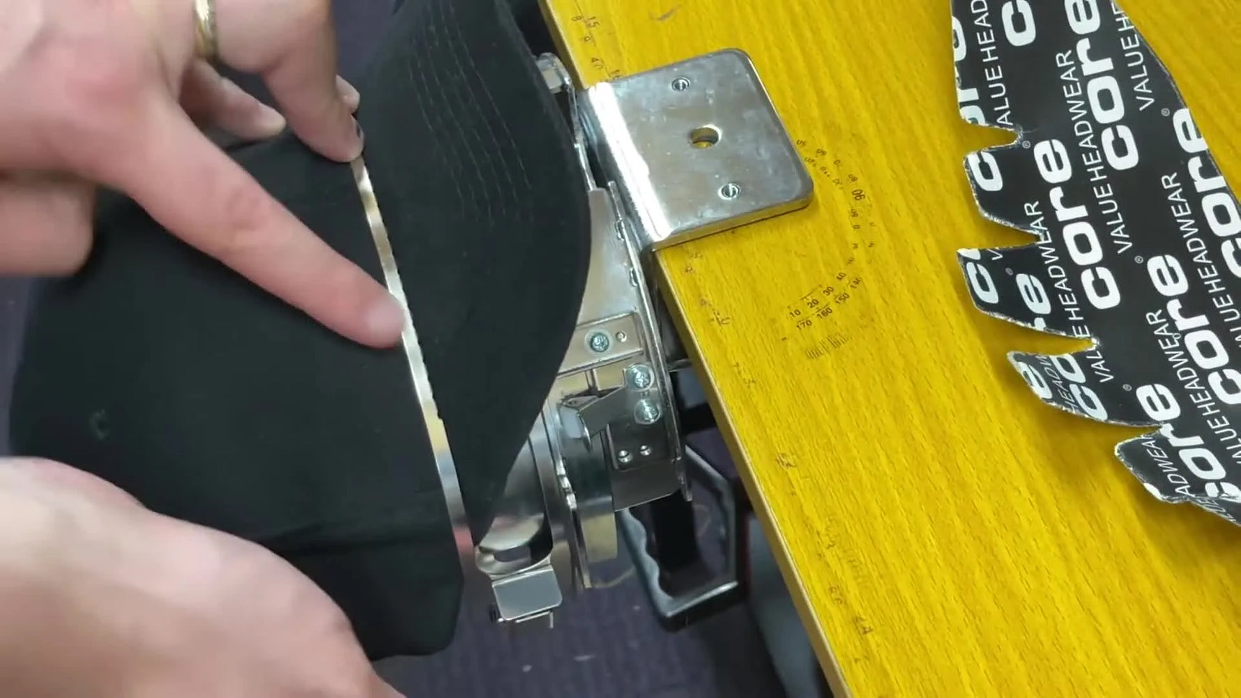 A close-up of the main clamp latch being closed to lock a structured baseball cap into a mechanical cap frame before loading onto a Brother multi-needle machine.