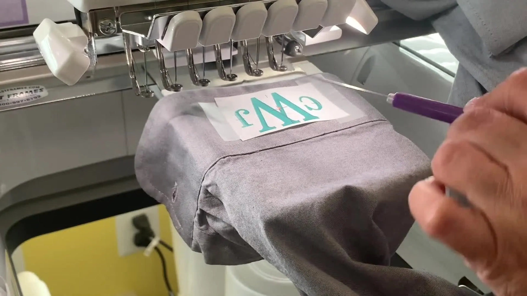 A close-up shows the machine’s red laser dot landing exactly on the printed template crosshair taped to a dress shirt cuff for perfect monogram centering.
